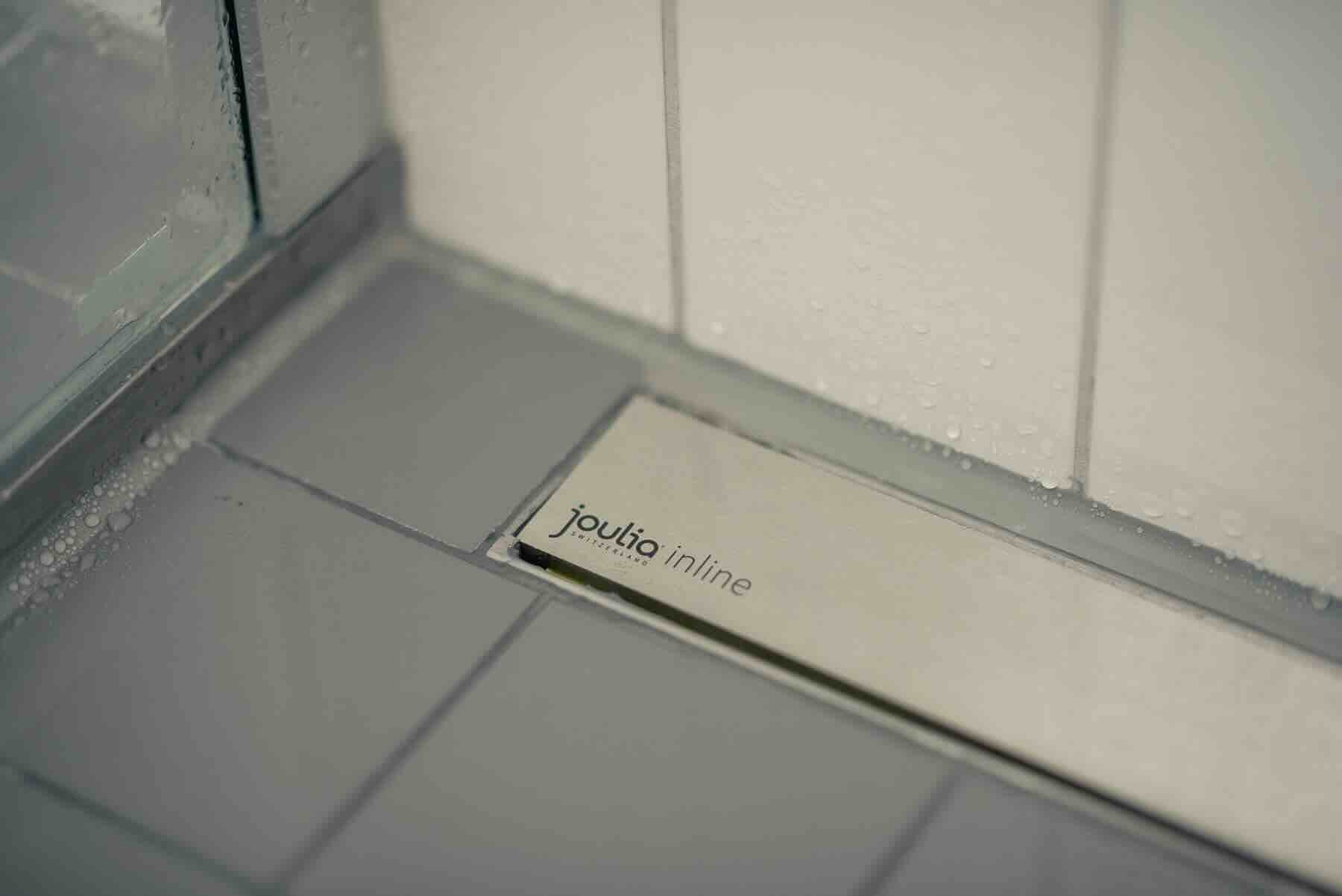 Nahaufnahme einer Inline-Duschrinne mit Wärmetauscher, integriert in gefliesten Duschboden für effiziente Energienutzung