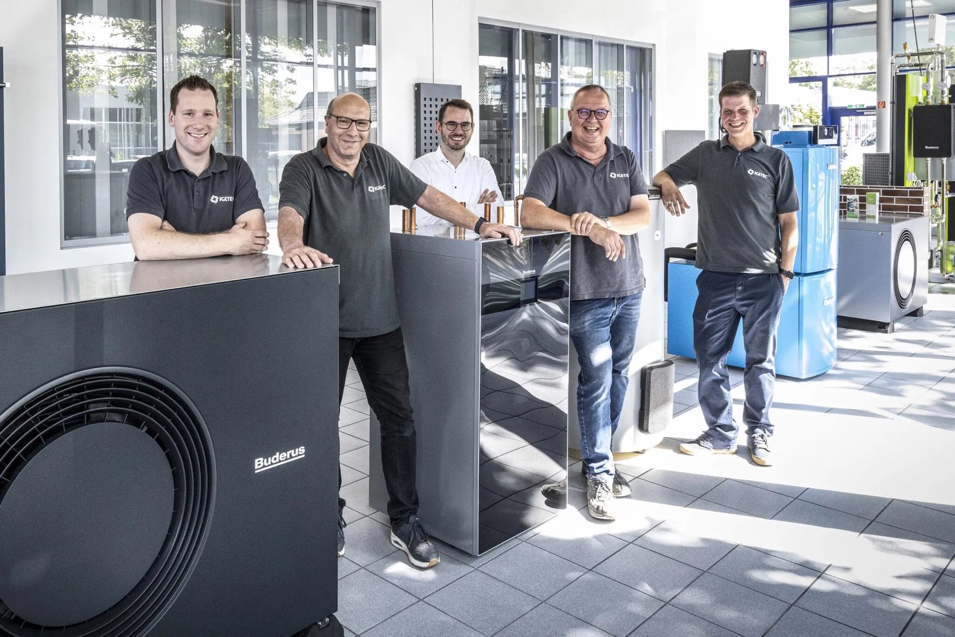 Team von IGETEC Energie- und Umwelttechnik in moderner Technikhalle mit Heizungs- und Gebäudetechniksystemen – Spezialisten für energieeffiziente Lösungen in Heizung, Sanitär, Klima und Lüftung.