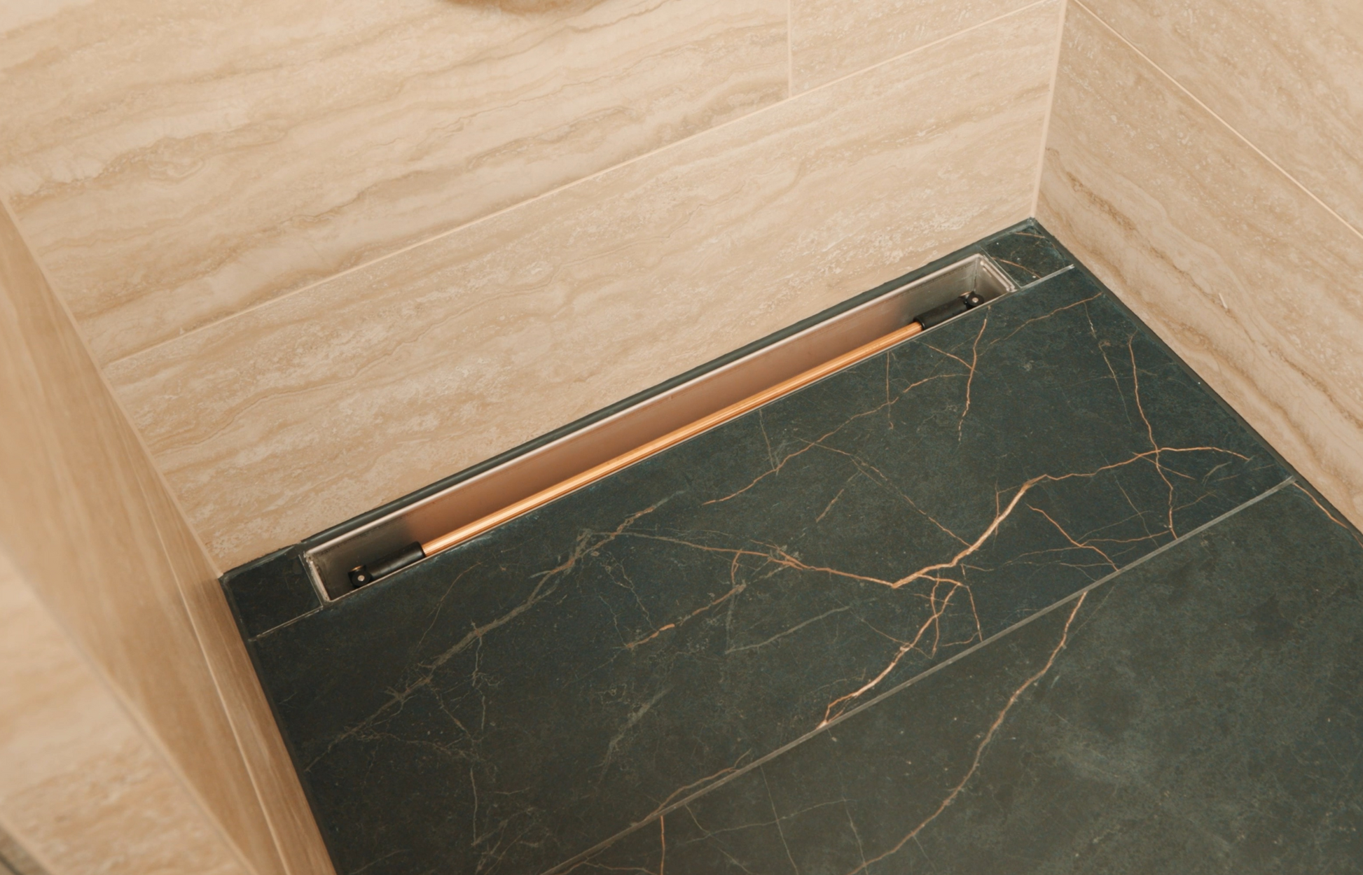 Bodenebene Inline-Duschrinne in einem modernen Hotelbad, dezent in dunkle Natursteinfliesen integriert und entlang der Wand platziert