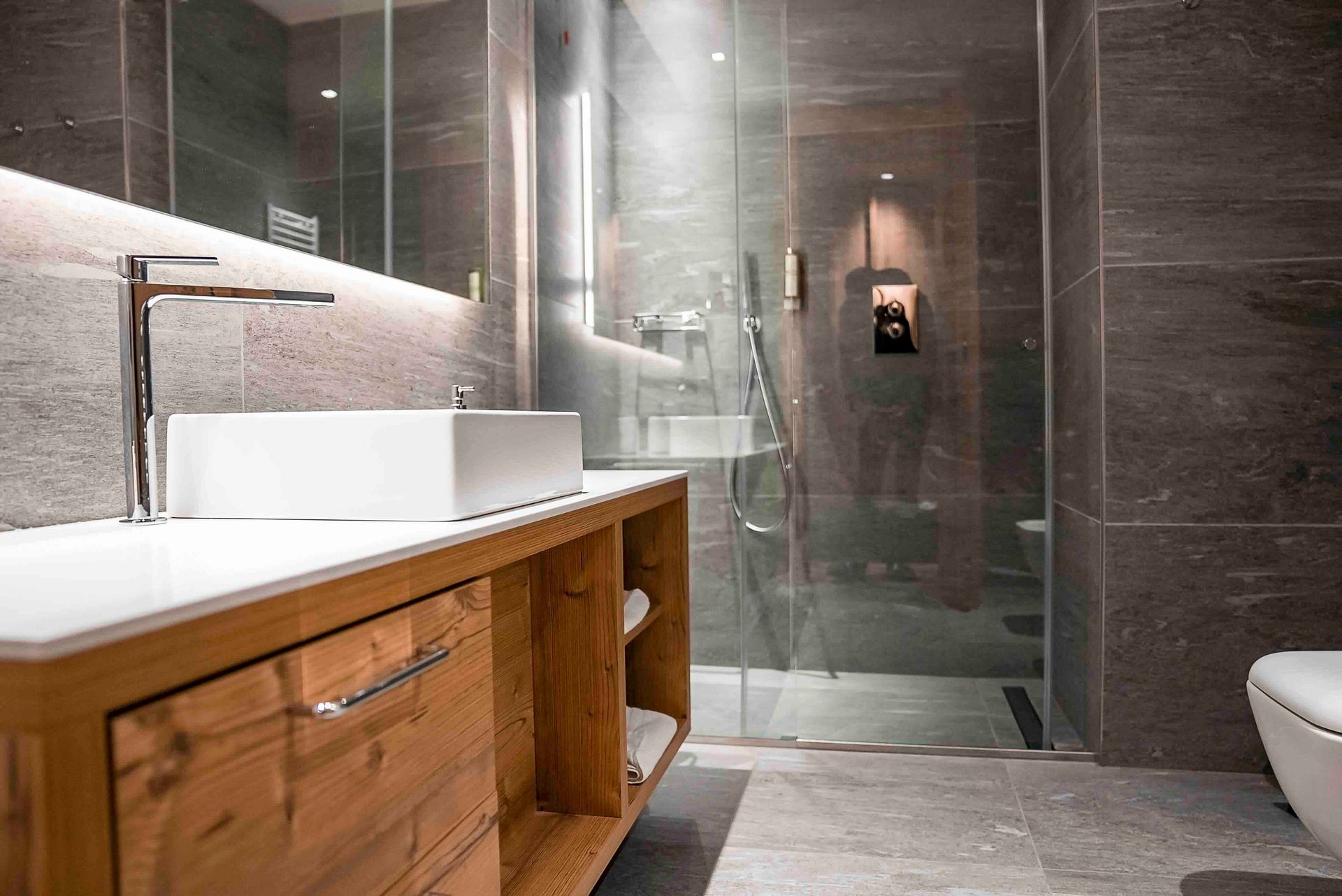 Modernes Badezimmer mit hochwertiger Sanitärinstallation, Waschtisch aus Holz und bodengleicher Dusche – Der Haustechniker: Fokus auf individuelle Planung, Ästhetik und langlebige Technik.