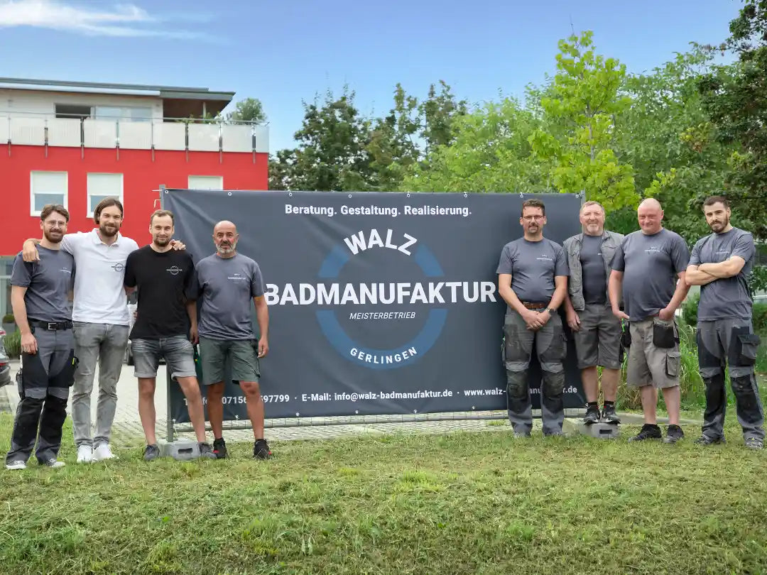Team der Walz Badmanufaktur steht gemeinsam vor einem Firmenbanner im Außenbereich – erfahrener Meisterbetrieb aus Gerlingen für Teil- und Komplettbadsanierungen, Sanitär, Fliesen, Elektro- und Koordinationsarbeiten als Unocconi Partnerbetrieb.