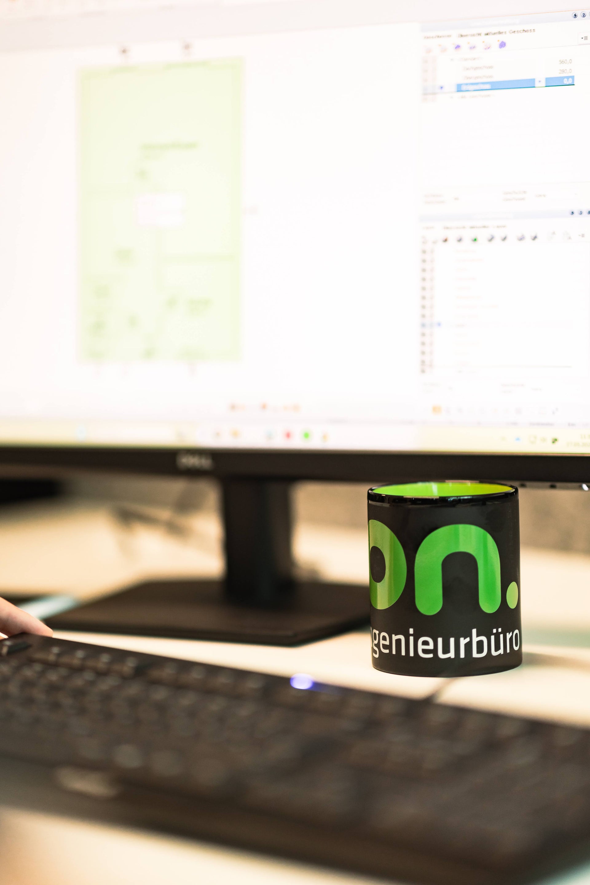 Arbeitsplatz des on. ingenieurbüros mit Monitor, Tastatur und gebrandeter Tasse im Vordergrund, symbolisiert digitale Planung, effiziente Prozesse und unabhängige Energie- und Bauingenieurberatung